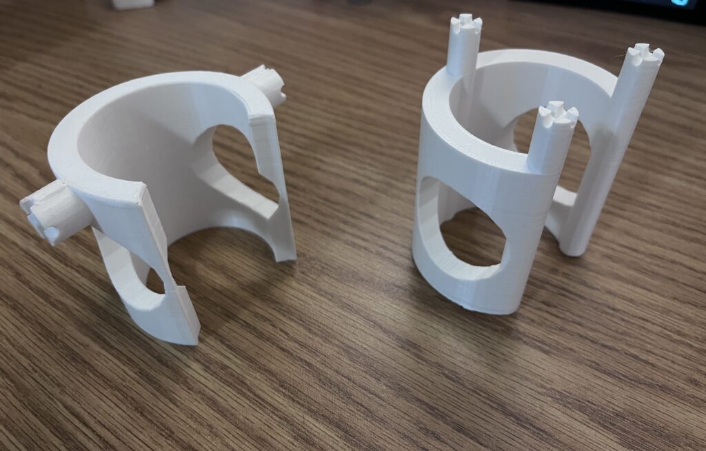 3D prints of Design 3.0 on the left and Design 3.1 on the right. The models are cylindrical shaped and have knobs coming from the sides and top.