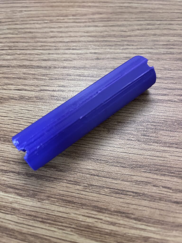 3D print of Design 4.0. A purple cylinder with cross divots on each side.